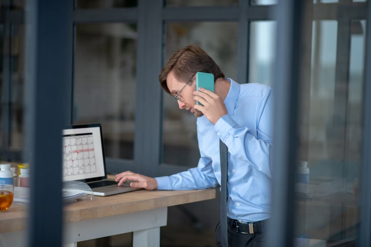 Gerente de una empresa habla por teléfono mientras consulta los turnos de trabajo en su ordenador