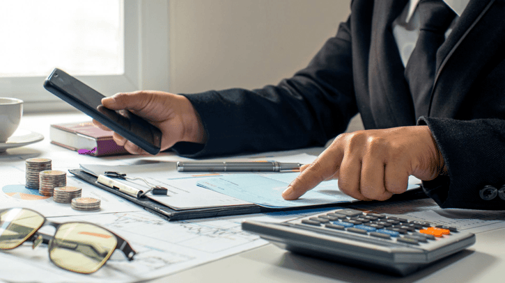 Ein Arbeitgeber überprüft eine Finanztabelle, die die Gehälter und Abzüge der Mitarbeiter zur Berechnung des Nettoeinkommens anzeigt, wobei er die Zahlen in einem hellen, modernen Büro mit einem Stift hervorhebt -  Haushalte
