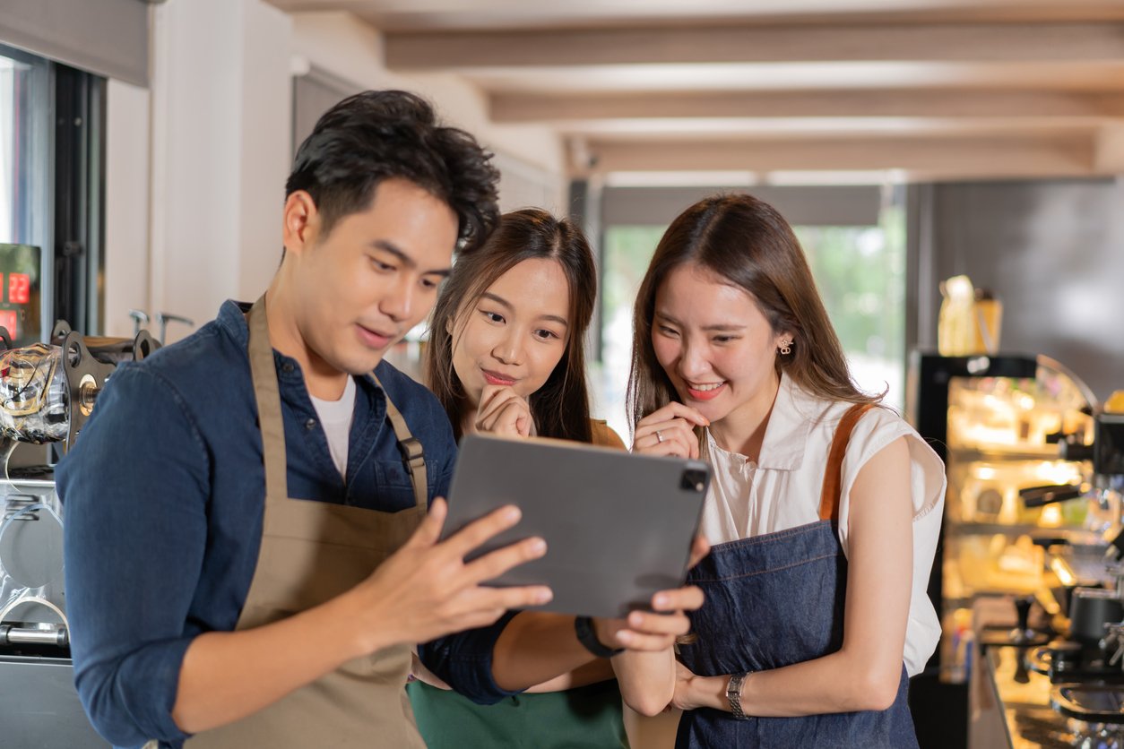 Un equipo de cafetería asiática formado por tres personas revisando su horario de trabajo mostrado en una tableta.