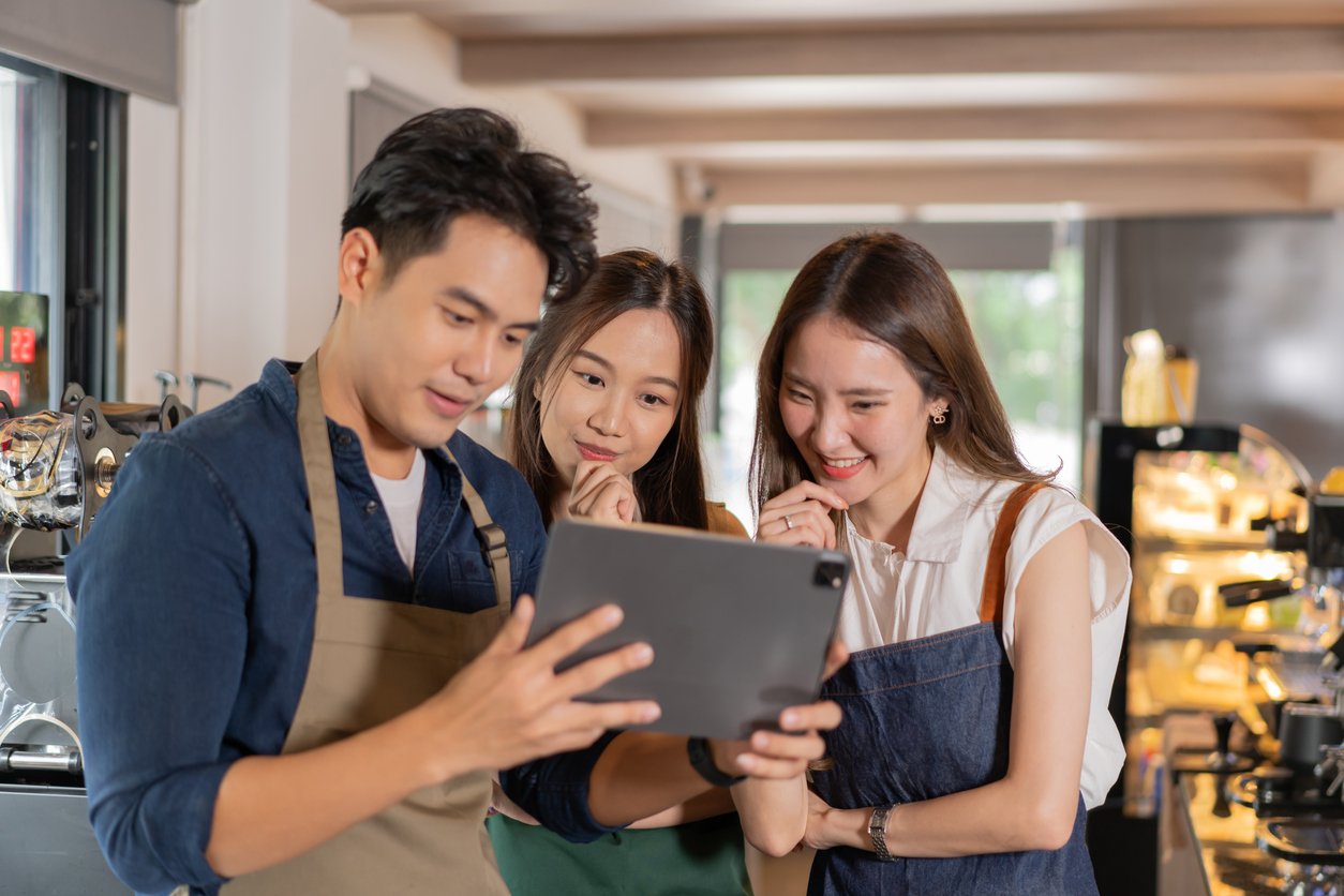 An asian coffee shop team of three people reviewing their work schedule displayed on a tablet.