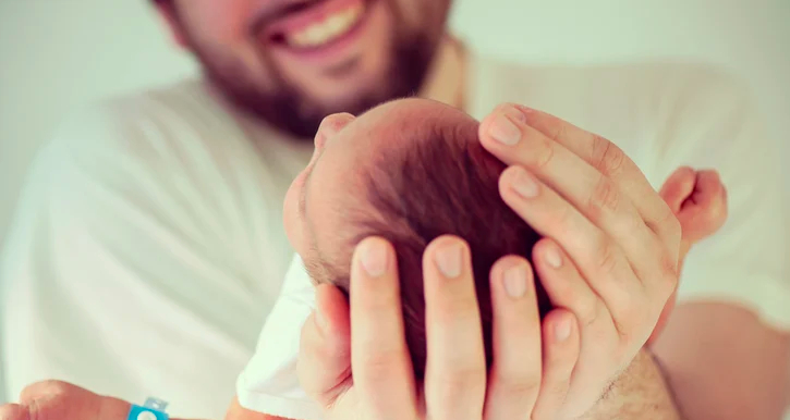 Vooraanzicht, man houdt baby's hoofd  vast in zijn handen en glimlach