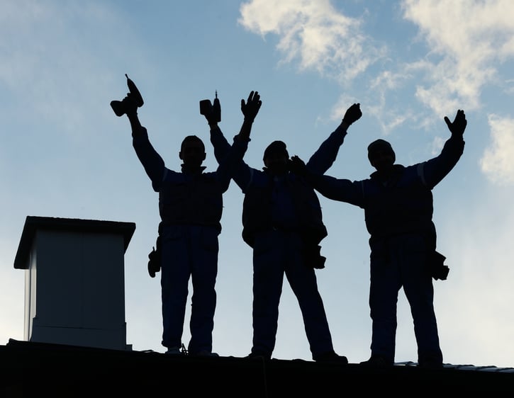 bouwvakkers die op het dak staan met hun armen in de lucht