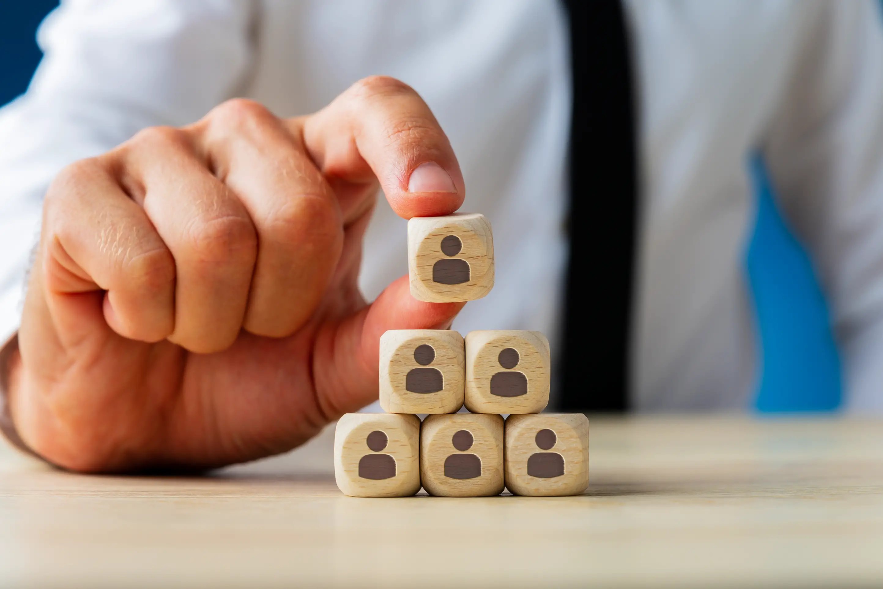 Business executive stacking wooden dices with people icons on them in a pyramid shape, symbolising organizational structure, hierarchy or organigram