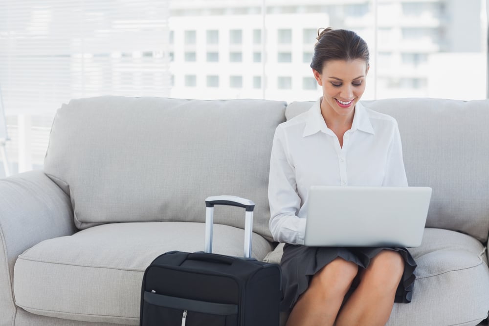 Femme d'affaires assise sur le canapé, utilisant son ordinateur portable à côté de sa valise