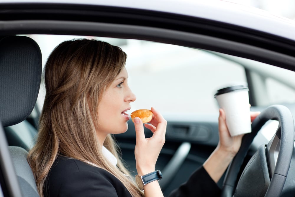 Charming businesswoman eating and holding a drinking cup while driving to work