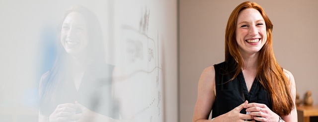 Vrouw met rood haar staat lachend voor whiteboard