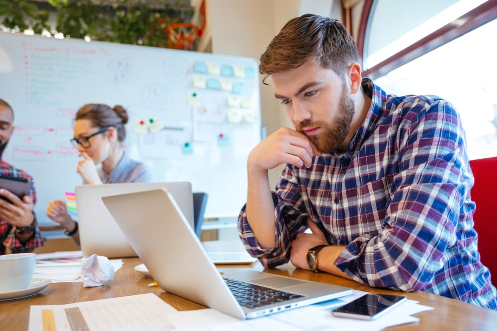 Concentrated bearded young man using laptop while his friends studying together-1