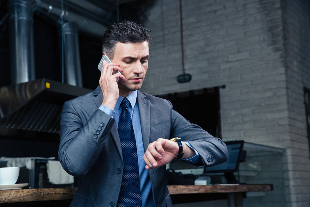 Confident businessman speaking on the phone and looking on the wristwatch in cafe-2