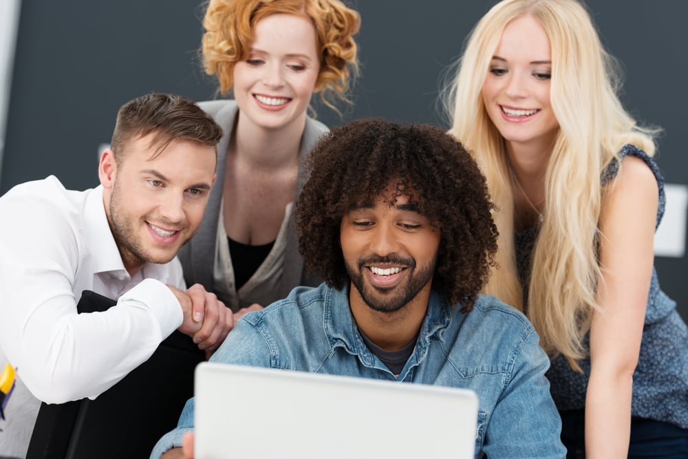 Creative multiethnic young group of business partners working together on a laptop computer grouped around a smiling African American man