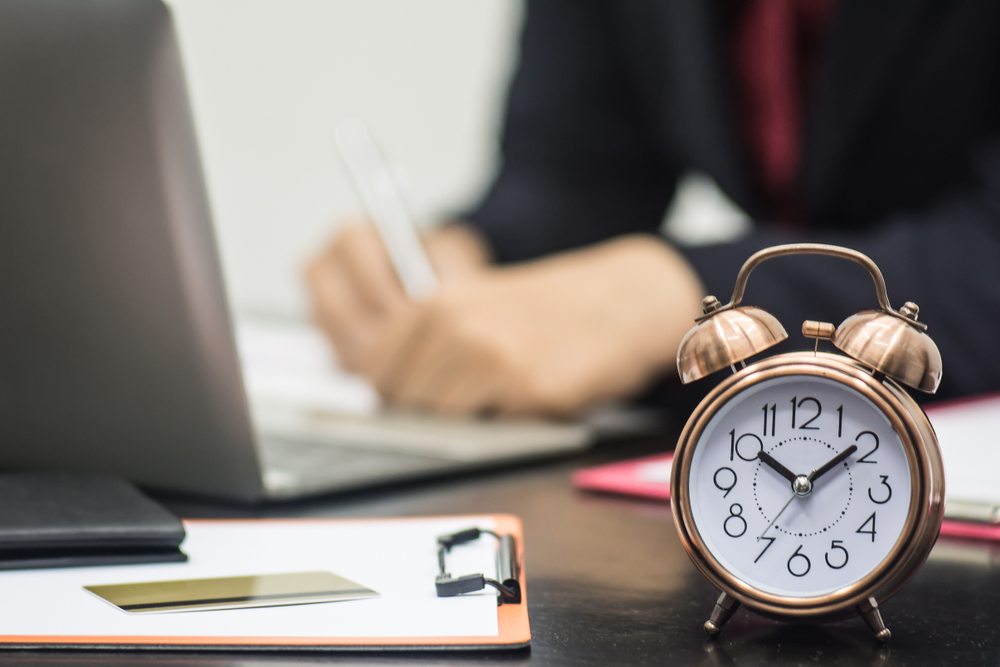 Creative shot of focused clock with business employee working behind laptop in the background