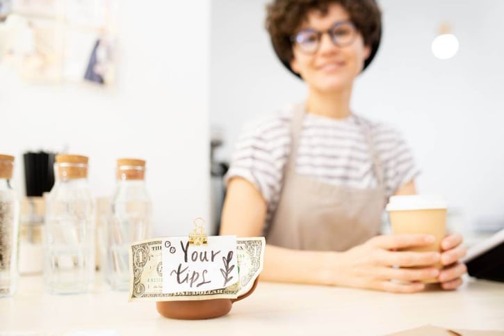 Cup with tag Your tips with cafe employee in the background, tip credit