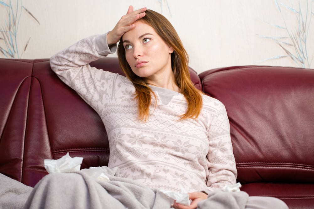 Cute lovely pregnant woman in pink pajamas having headache sitting on couch at home