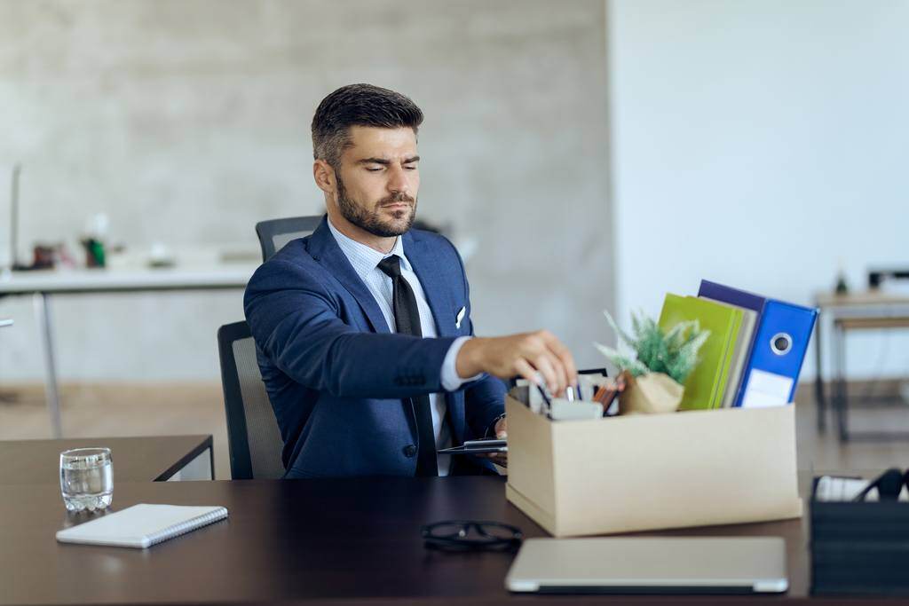 Demoted businessman packing up his belongings from the desk symbolising demotion at work 
