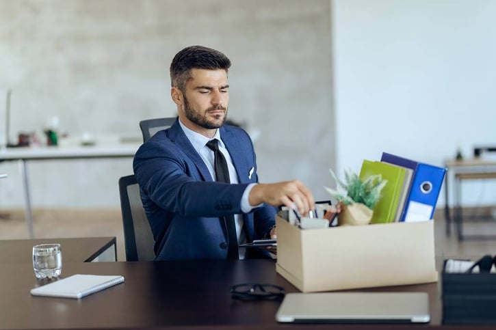 Demoted businessman packing up his belongings from the desk symbolising demotion at work