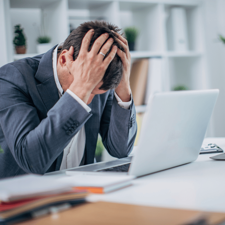 Werknemer heeft demotie gekregen en hangt met zijn hoofd in zijn handen voor zijn laptop