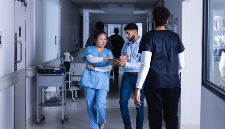 Doctors discussing on-call schedule using tablet while walking in hospital corridor