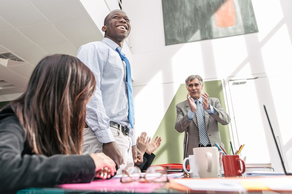 Employees clapping in office for promoted standing employee