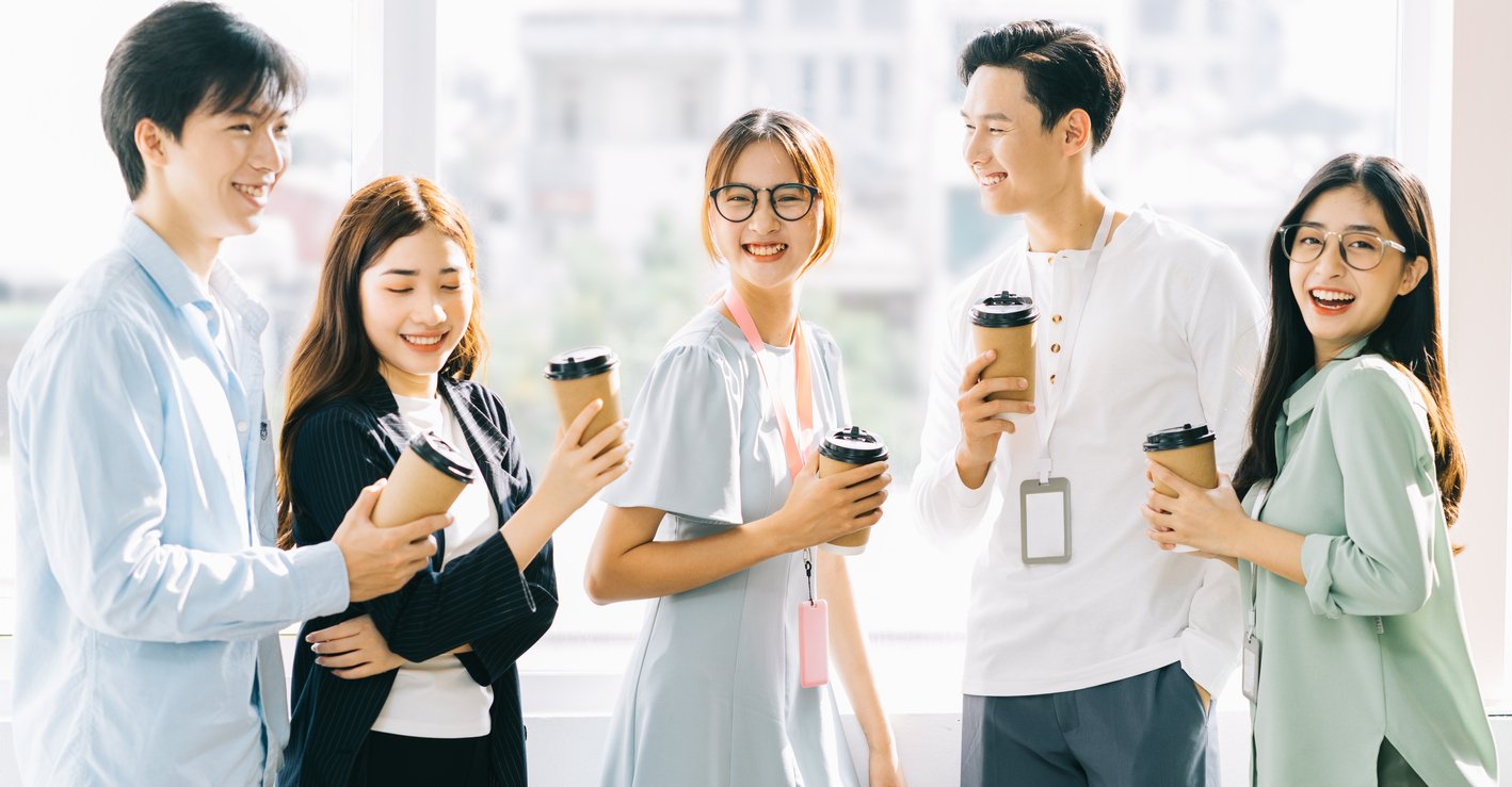 Group of asian business people chatting and drinking coffee to suggest coffee badging in a hybrid workplace