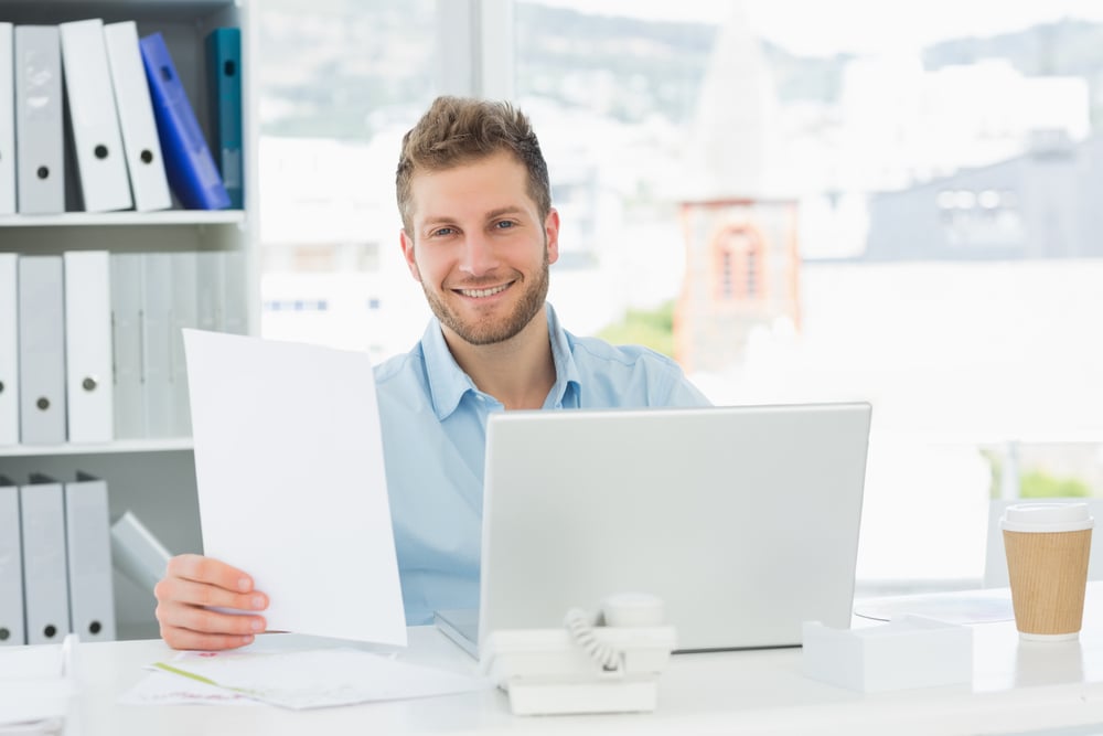 Handsome man working at his desk on laptop smiling at camera in creative office