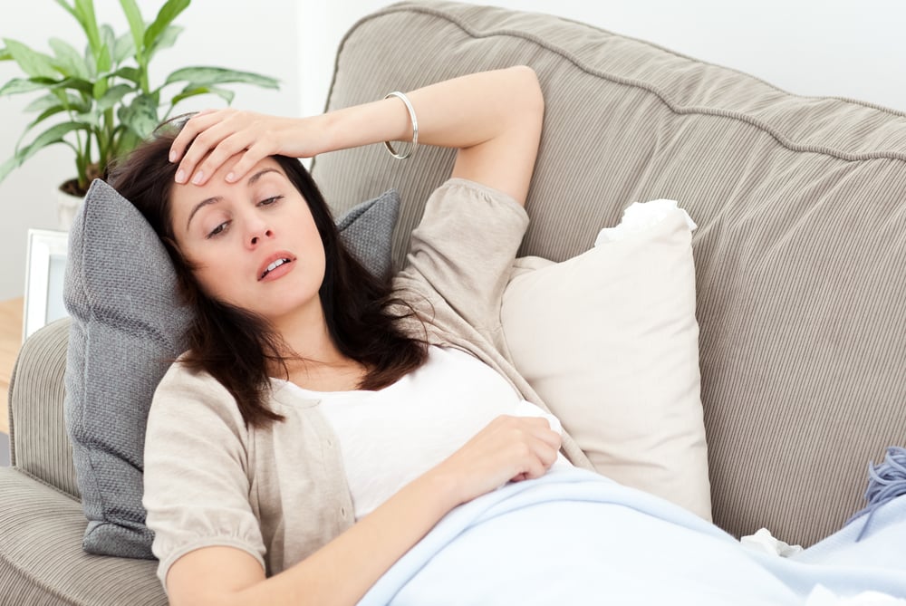 Indisposed woman feeling her temperature while resting on the sofa at home-1