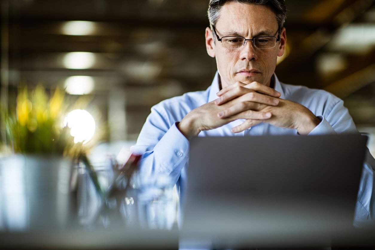 Male hiring manager in his office with glasses looking intently at laptop and in deep though