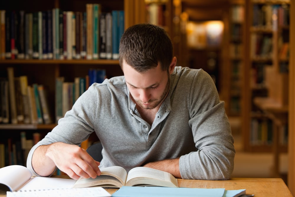 Male student researching with a book in a library