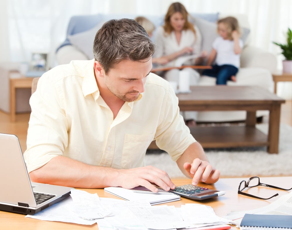 Man calculating his bills while his family are sitting on the sofa-2