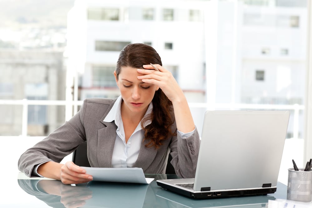 Pensive businesswoman looking at a paper while working on her laptop at her desk