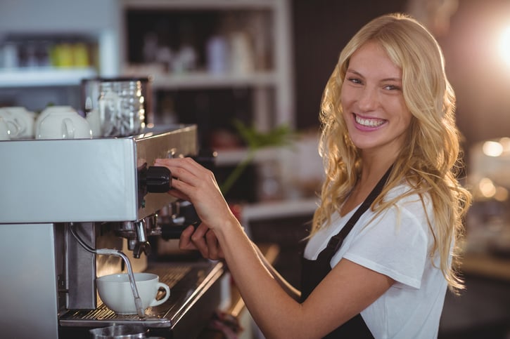 Portrait of smiling waitress making cup of coffee in cafe