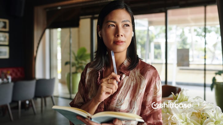 Werkgever denkt na met pen tegen haar kin en notitieboek open, voor de vaardigheden van haar personeel en wie ze kan inzetten