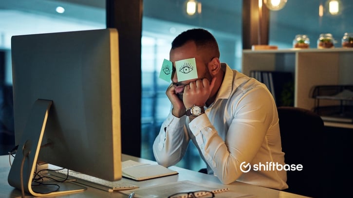 Werknemer achter een computerscherm met post its op zijn ogen met ogen erop getekend vanwege vermoeidheid