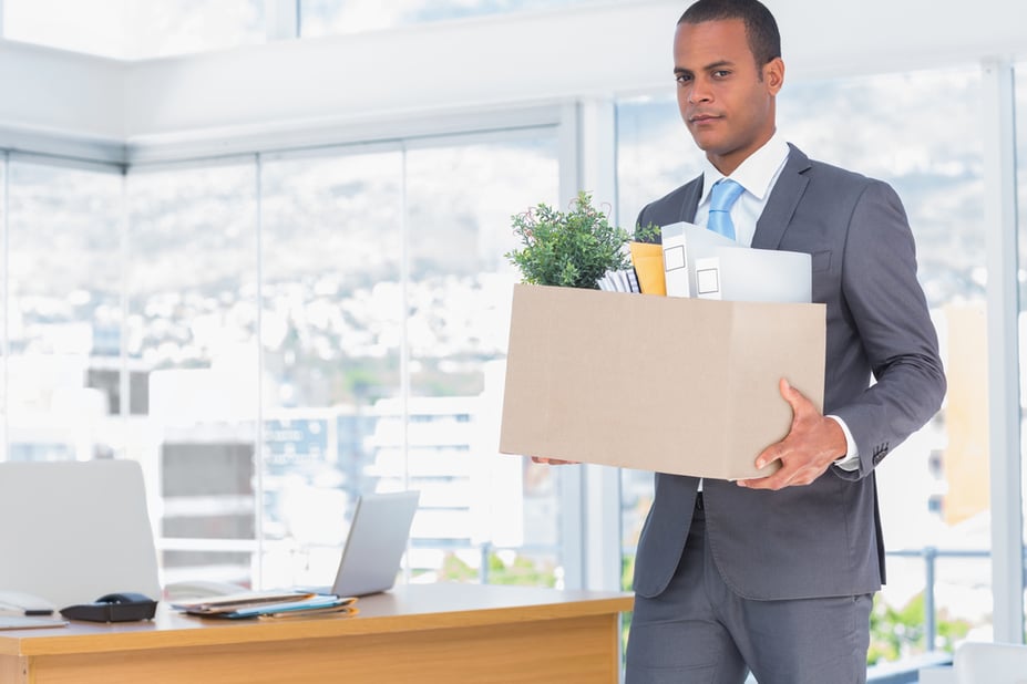 Ein Mitarbeiter verlässt leise das Bürogebäude mit einer Box persönlicher Gegenstände, Symbol für stille Kündigung.