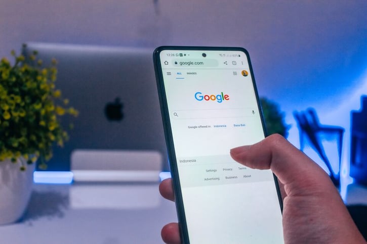 Beeld van iemand die op google zit op zijn telefoon. Alleen de telefoon en de duim zijn in beeld.