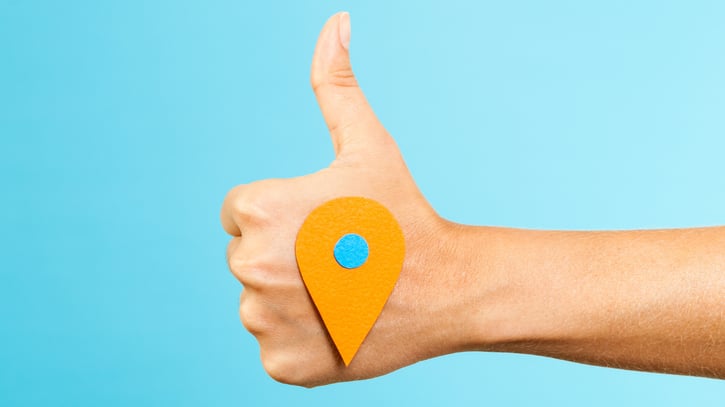 Pulgar apuntando hacia arriba con el signo de ubicación que simboliza la geolocalización como concepto.