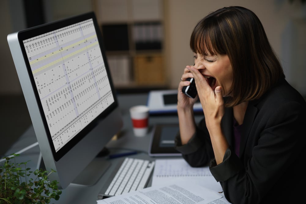 Tired Businessman at her Desk, Showing Yawning Gesture While Talking to Someone on Mobile Phone.