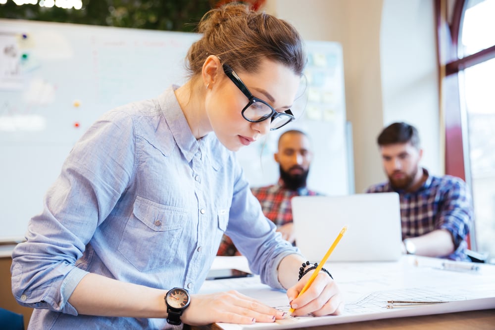 Woman engineer working on blueprint in office with colleagues on background-3