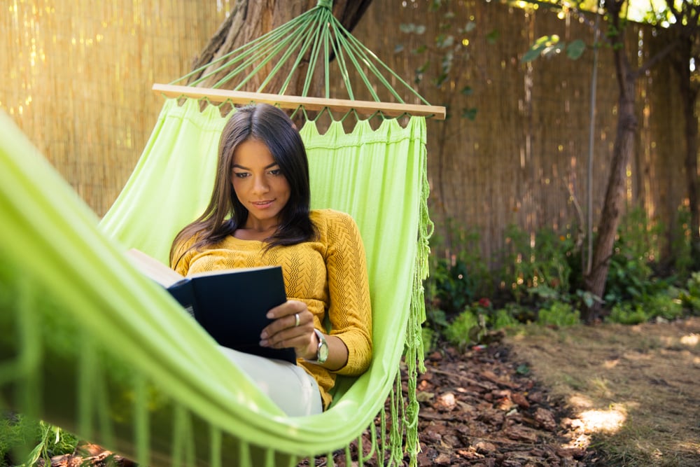 Woman lying on hammok and reading book outdoors