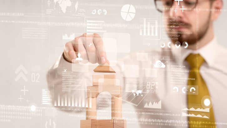 Young handsome businessman using wooden building blocks with mixed data around him