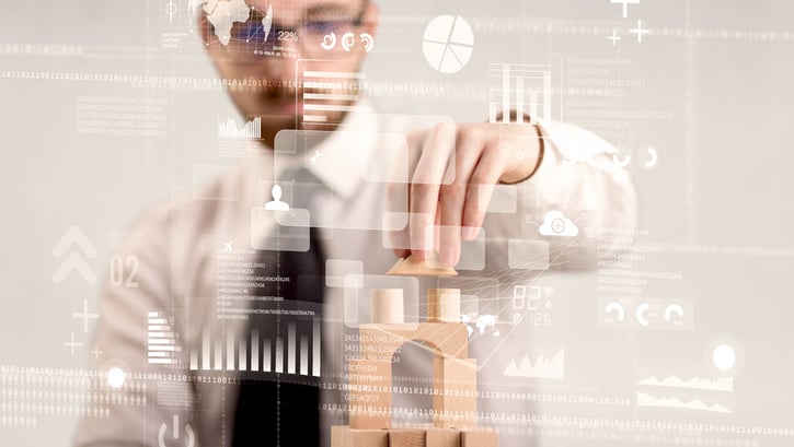 Young handsome businessman using wooden building blocks with mixed data around him symbolising digital workplace