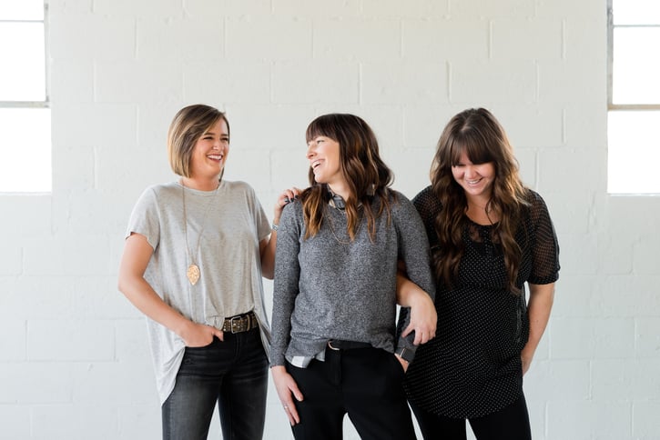Vrouwen staan voor witte muur en lachen vriendelijk