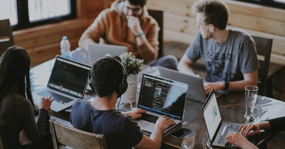 Collega's zitten samen aan tafel met laptops voor zich