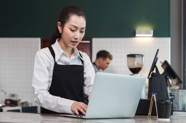 Busy asian young women barista wearing apron using laptop