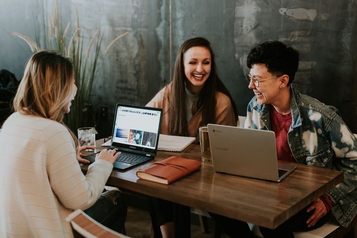 Collega's zitten aan een tafel voor laptops en lachen naar elkaar