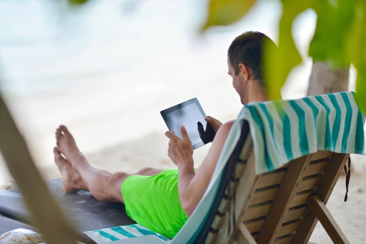 Man ontspant in een strandstoel op het strand en kijkt naar een iPad