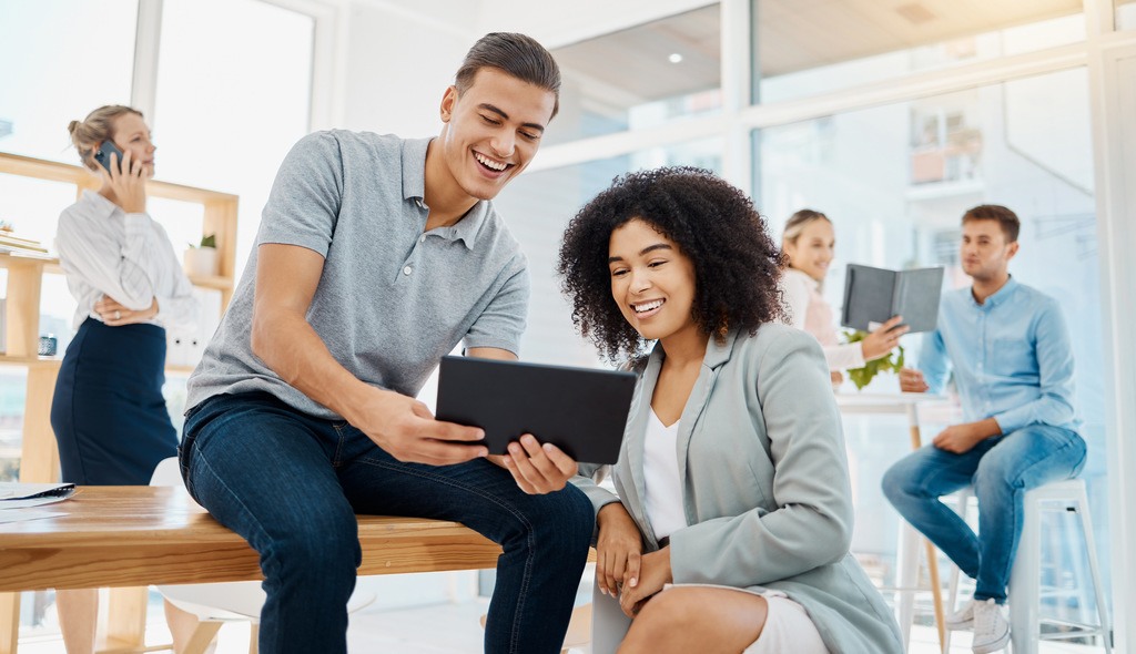 two happy employees in the workplace looking at data on a tablet 