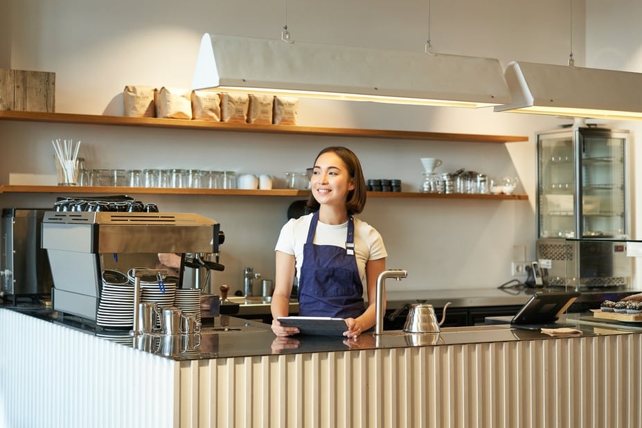 coffee shop manager or barista standing behind bar with iPad in hand