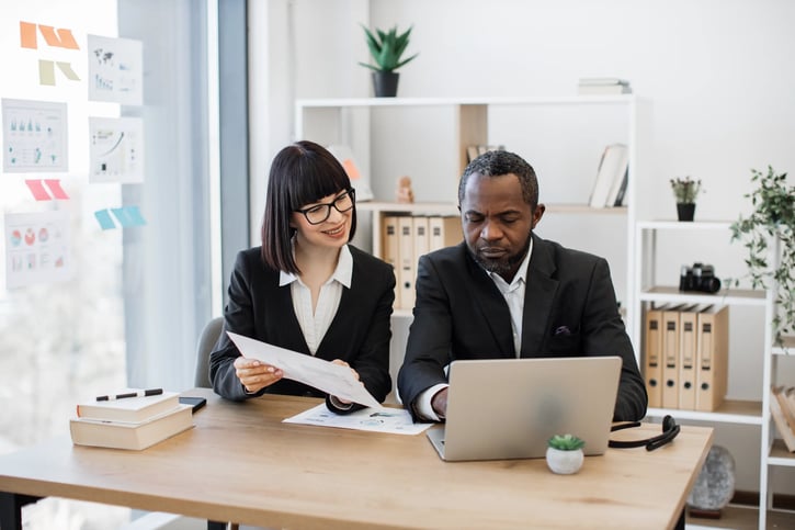 colleagues comparing data on paper and laptop