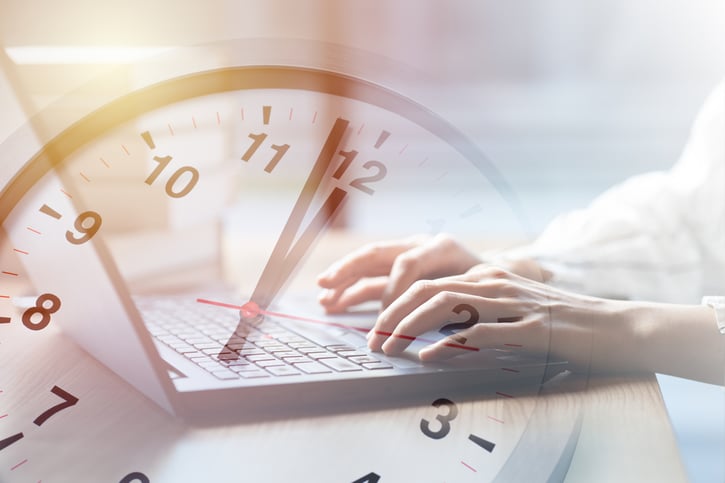 creative shot of clock with employee hands working on laptop in the background