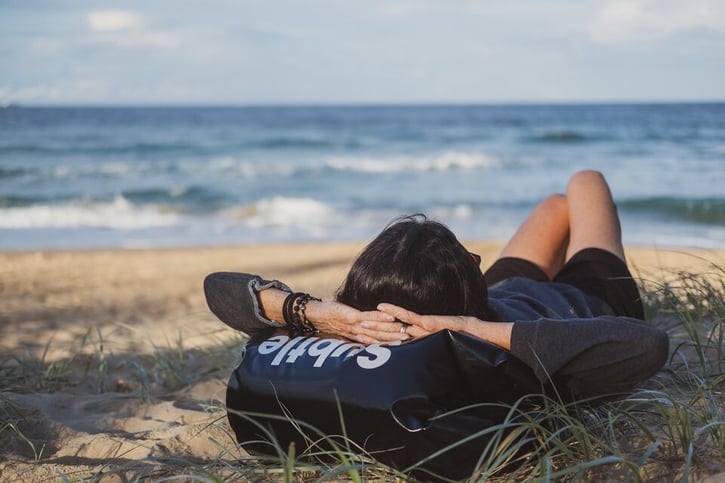 Women laying on the beach. She's using her bag as a pillow.
