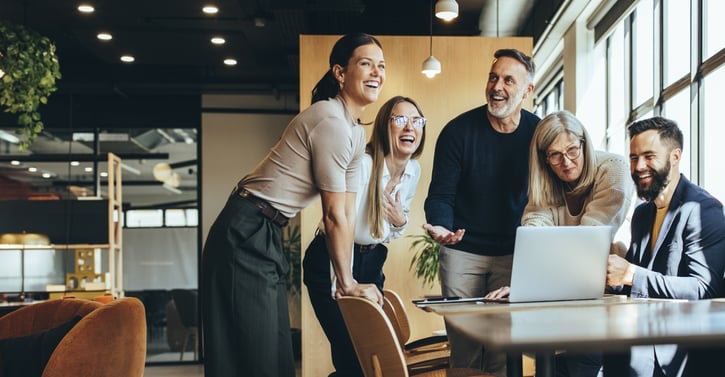 Mitarbeitende lachen während einer Besprechung, was die Merkmale des glücklichen Betriebsklimas während der Arbeitswoche des Betriebes zeigt und Arbeitsunlust mindert.